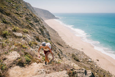 Woman hiking on mountain by sea during sunny day