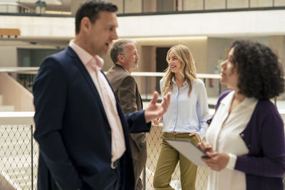 Smiling businesswoman by businessman with colleagues discussing in foreground at office