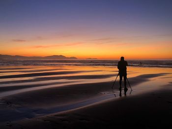 Silhouette people standing on beach against sky during sunset