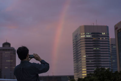 Rear view of man photographing against sky at sunset