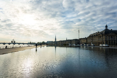 Garonne river by buildings against cloudy sky