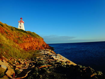 Lighthouse by sea against clear sky