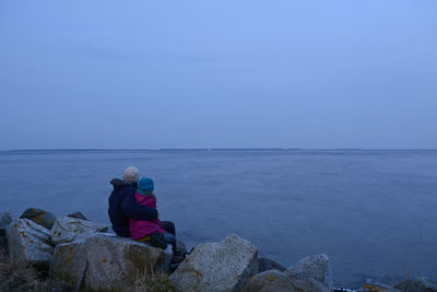 Rear view of mother and daughter on rocks at beach