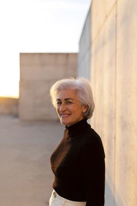 Smiling mature woman standing by wall