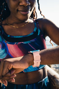 Crop african american female wearing sportswear checking health indicators on tracker after outdoor workout in sunny day