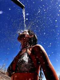 Low angle view of woman taking shower against clear sky during sunny day