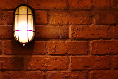 Close-up of illuminated light bulb against brick wall