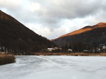 Scenic view of frozen lake by mountains against cloudy sky