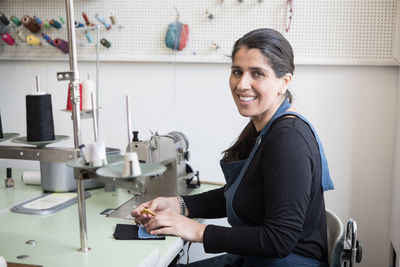 Portrait of smiling mature female tailor sitting by sewing machine at laundromat