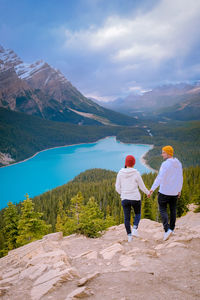 Rear view of friends holding hands on mountain against sky