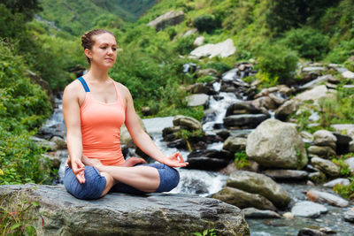 Full length of woman mediating on rock