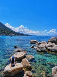 Rear view of woman sitting on rock by sea