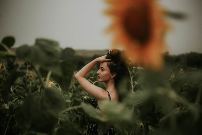 Young woman standing amidst sunflowers on field