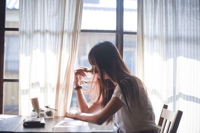 Woman using phone while sitting on window