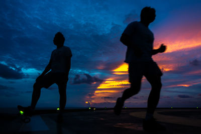 Silhouette friends standing against sea at sunset