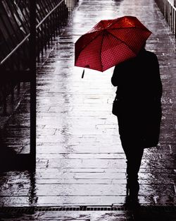 Rear view of woman walking on wet umbrella during rainy season