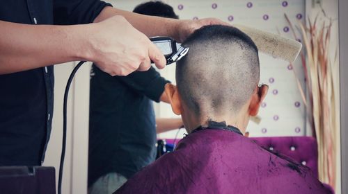 Midsection of barber cutting boy hair in shop