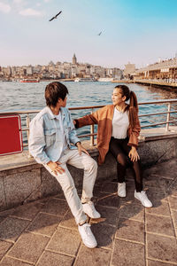 Full length of couple sitting on shore against sky