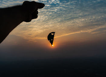 Silhouette person holding sun against sky during sunset