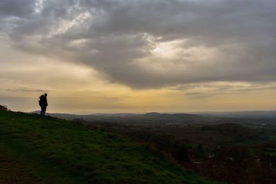 Silhouette man standing on field against sky at sunset