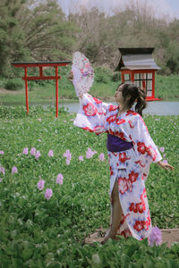 Woman wearing kimono holding hand fan while standing in park