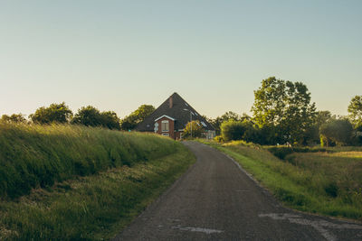 Road amidst trees and houses against clear sky