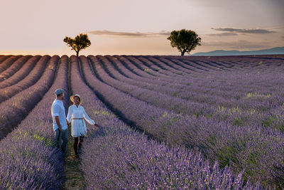 Rear view of woman walking on field against sky during sunset