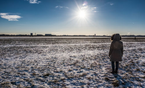 Rear view of woman standing on snow covered field against sky during sunny day