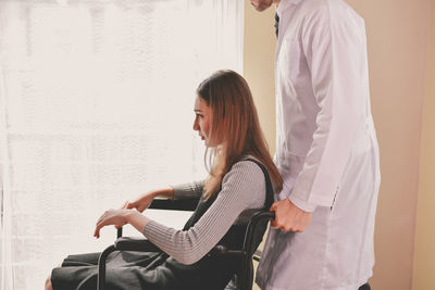Doctor pushing wheelchair with female patient sitting at clinic