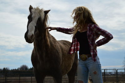 Woman with brown horse standing on field