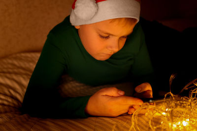 Boy holding phone in his hands in the dark with bright included christmas decorations.