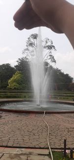 Cropped image of person by fountain against sky