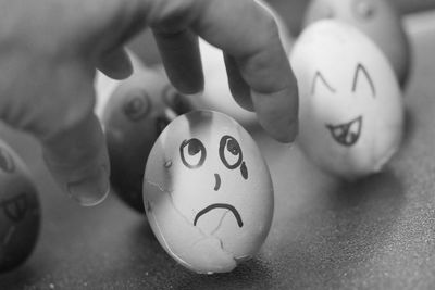 Cropped hand reaching towards face drawn ester egg on table