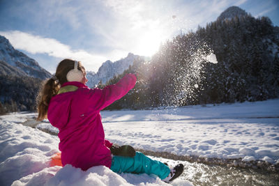 Side view of girl throwing snow against sky during winter