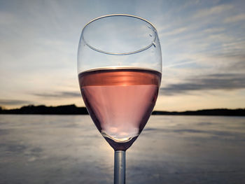 Glass of rose wine held up to sunset over frozen lake