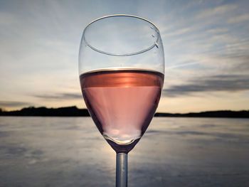 Close-up of glass of water against sky during sunset