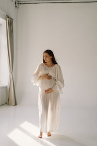 Cute young pregnant girl sitting on the white studio in warm light