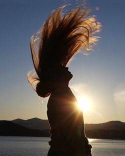 Side view of silhouette woman tossing hair against sky during sunset