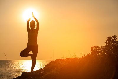 Silhouette woman doing yoga by sea against sky during sunset