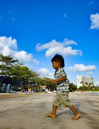 Side view of boy walking at beach against blue sky