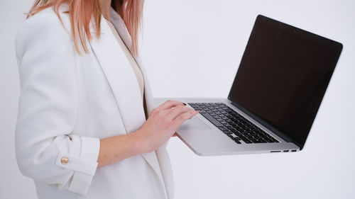Midsection of woman using laptop while standing against white background
