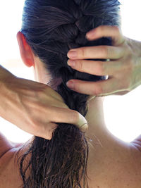 Rear view of woman braiding her hair against white background