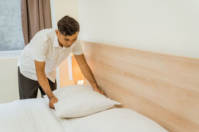 Side view of woman sitting on bed at home