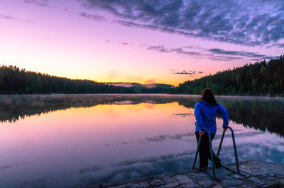 Rear view of woman standing at lake against sky during sunset