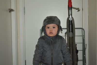 Portrait of cute boy wearing jacket standing against closed door