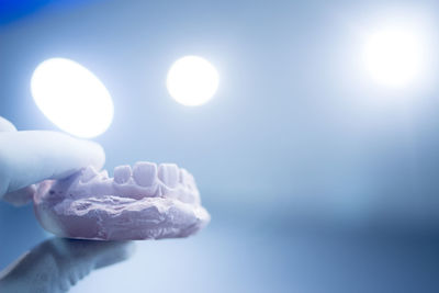 Close-up of hand holding dental mold against illuminated lights