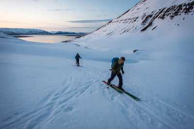 Man and woman backcountry skiing in iceland with water behind