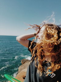 Cheerful woman with tousled hair by sea against clear sky