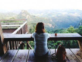 Rear view of woman sitting in balcony against mountains