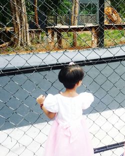 Rear view of girl standing by chainlink fence